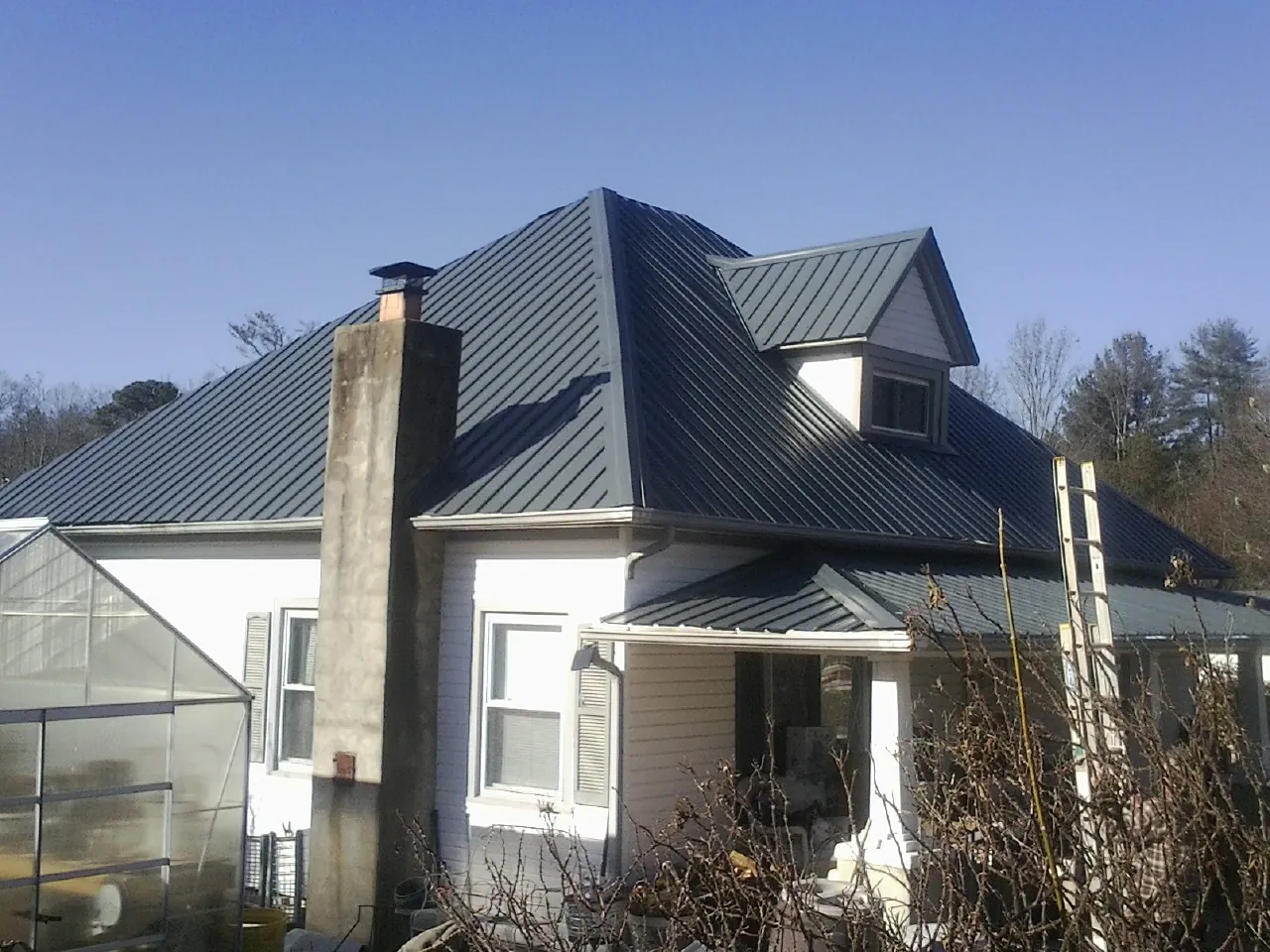 Dark blue standing seam metal roof on a white farmhouse with dormer — Slate & Tile Roof Repair by Roofing Brothers in Clintondale
