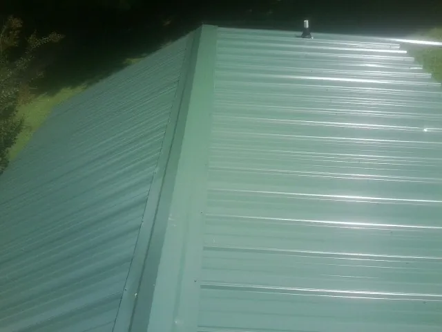 New green metal panels meeting at the ridge of a roof — Flat Roof Repair work by our crew in Clintondale