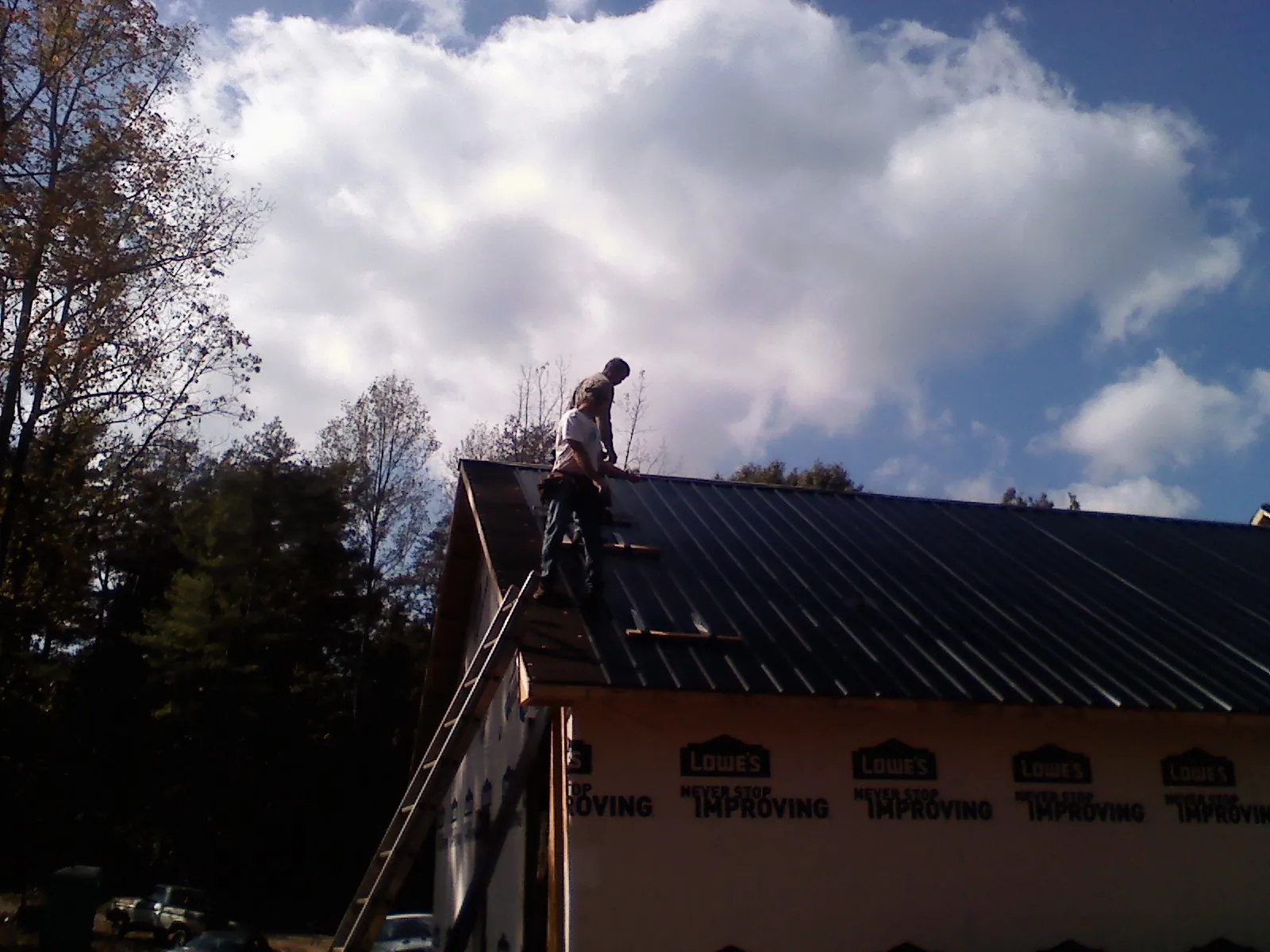 Roofer fastening dark metal panels high against a cloudy sky, from a Roof Inspection job in Clintondale