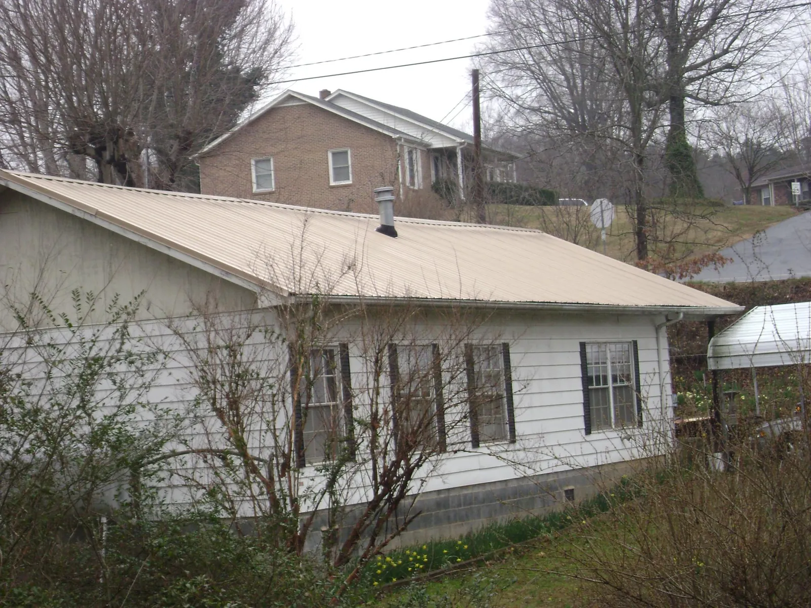 Tan metal roof on a white sided house set into a hillside — Commercial Roofing by Roofing Brothers in Clintondale